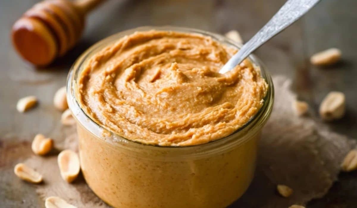 Homemade Honey Roasted Peanut Butter in a jar with peanuts and honey dipper