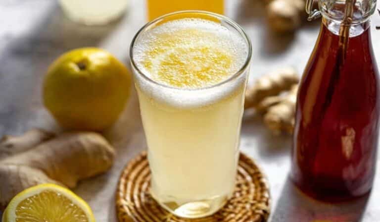 Homemade prebiotic ginger soda in a glass and bottle with lemon and ginger on marble.