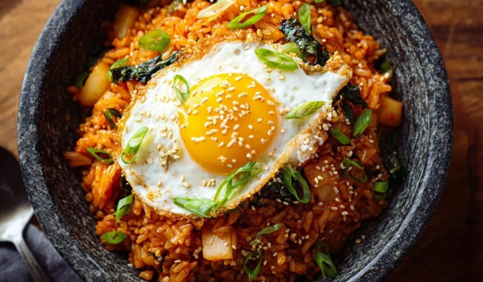 Kimchi fried rice topped with a fried egg and scallions in a black bowl