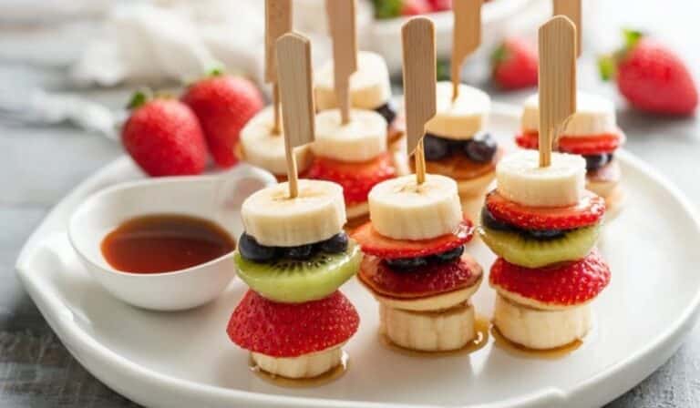 Mini pancake skewers with fruit on a brunch platter with maple syrup