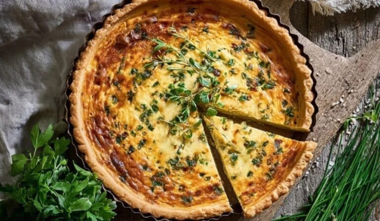 Quiche Lorraine with spring herbs in a tart pan on a wooden table